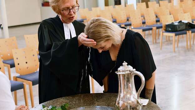 Pfarrerin Margit Zahn tauft eine junge Frau am Taufstein mit Wasserkanne Pfarrerin Margit Zahn tauft eine junge Frau am Taufstein mit Wasserkanne
