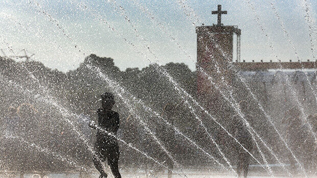 Menschen unter Wasserfontaine - im Hintergrund steht eine Kirche