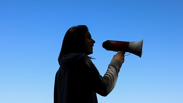 Junge Frau mit Megaphone vor blauem Himmel