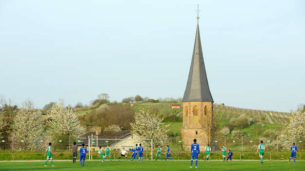 Fußballer spielen auf einem Sportplatz vor der Kulisse der evangelischen Kirche Oberöwisheim.