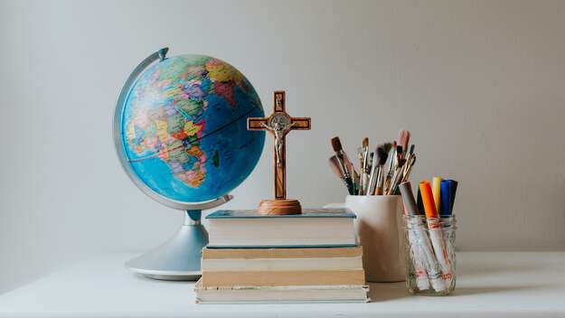 Schreibtisch mit einem Globus, einem Kreuz, Büchern und Stiften darauf