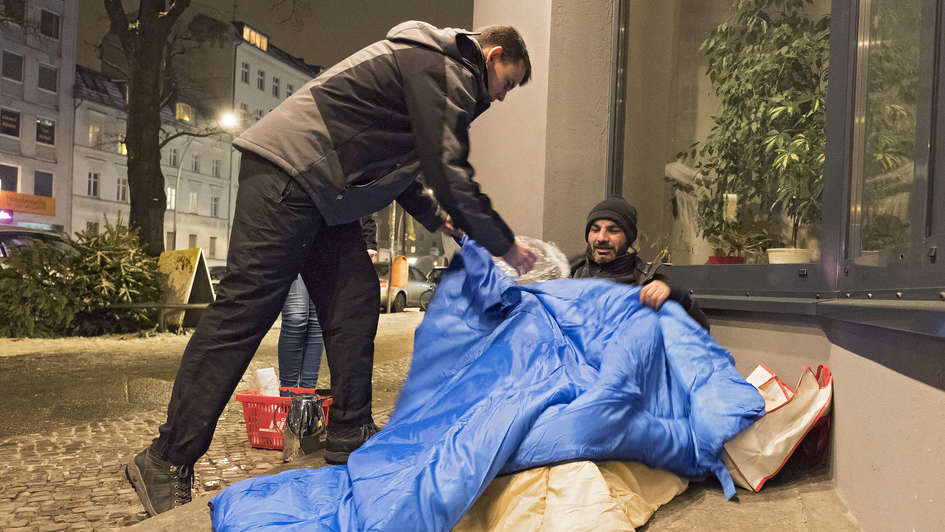 Fahrer des Berliner Kältebus gibt einem Obdachlosen einen Schlafsack