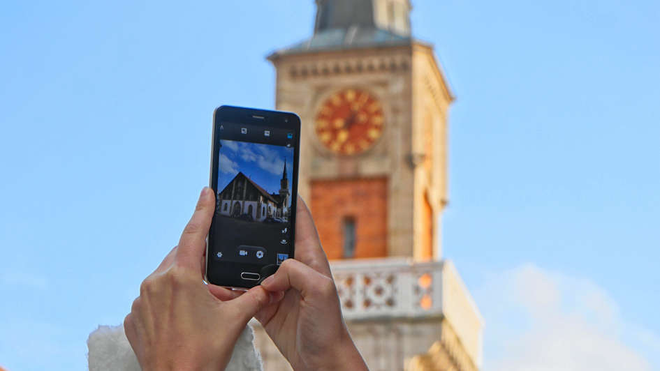 Smartphone vor einen Kirchturm gehalten, auf dem Dsiplay die Kirche