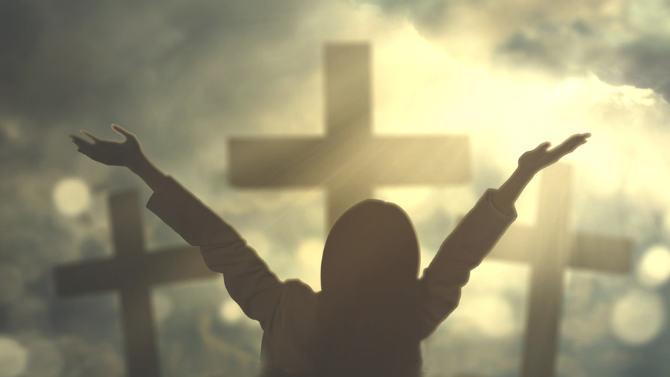 Eine Frau vor drei Kreuzen wirft die Hände zum Himmel
