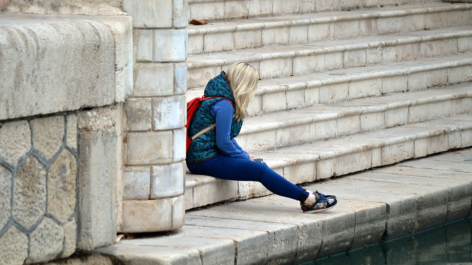 Junge Frau sitzt mit gesenktem Kopf auf Steinstufen