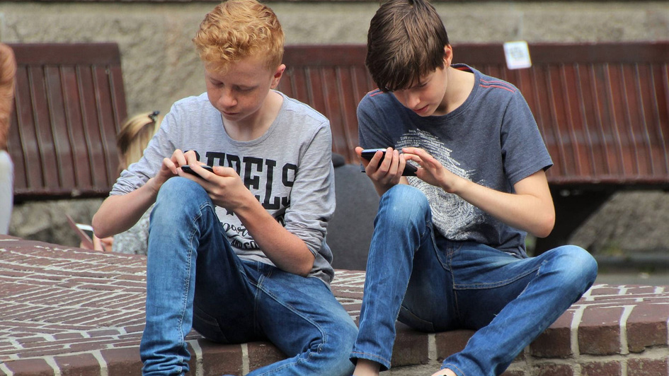 Zwei Jugendliche sitzen in ihre Smartphones vertieft nebeneinander