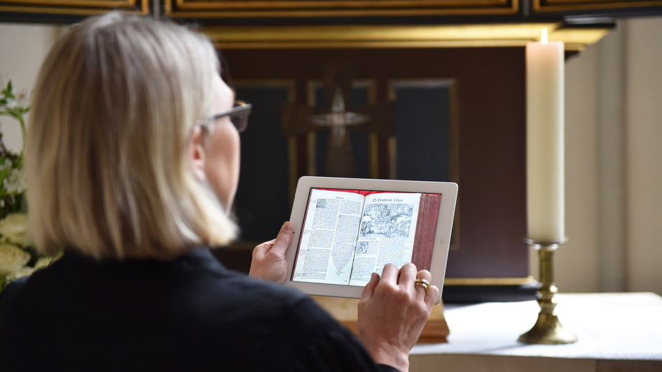Pfarrerin im Talar liest eine digitale Kopie einer historischen Bibel auf ihrem Tablet