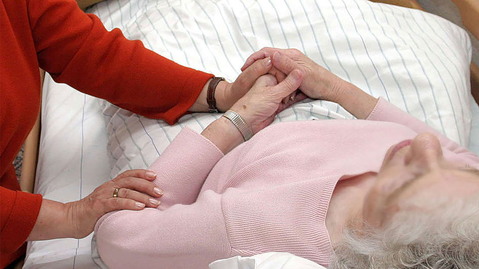 Eine ehrenamtliche Sterbebegleiterin am Bett einer Pflegeheimpatientin