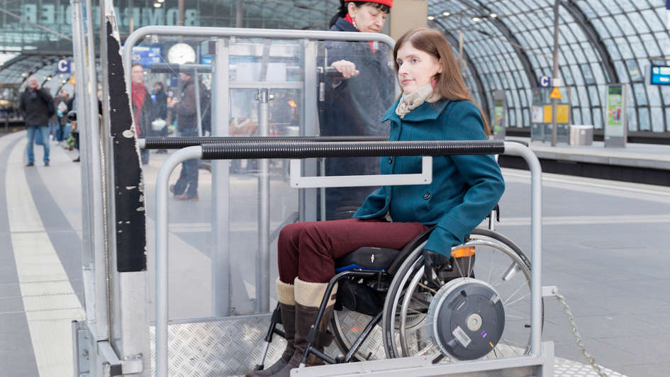Eine Frau im Rollstuhl fährt in einen Aufzug am Bahnsteig