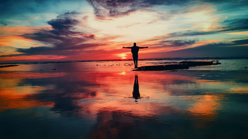 FriedensBibel - Mann steht am Strand und breitet die Arme gen Sonnenuntergang aus