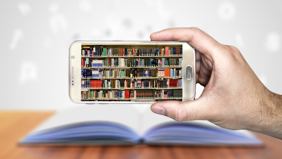 Eine Hand hält ein Smartphone hoch. Dieses ist auf ein aufgeschlagenes Buch gerichtet.  Auf dem Display des Smartphones ist eine ganze Bücherwand abgebildet.
