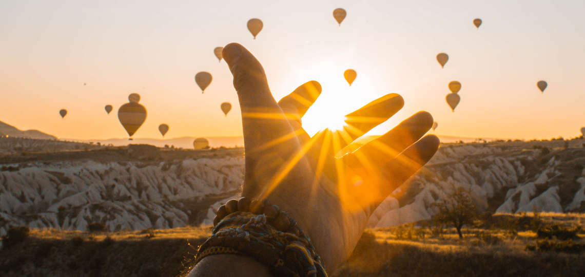 Hand im Sonnenaufgang und Heißluftballons im Hintergrund