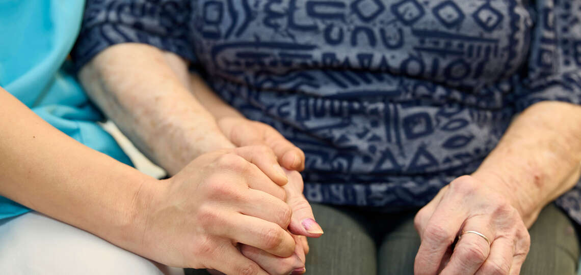 Themenbild Altenpflegeheimseelsorge: Pflegerin hält Bewohnerin die Hand