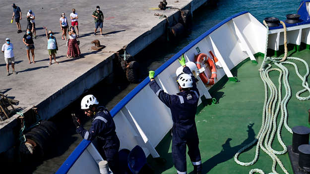 Crew-Mitglieder winken beim Auslaufen aus dem Hafen Zuschauern am Kai