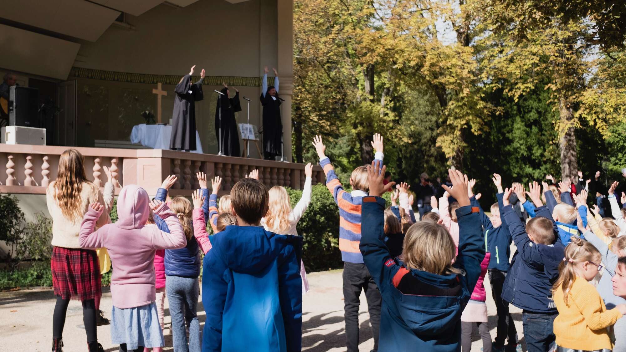 Bei einem Tauffest in Bad Homburg stehen Kinder mit erhobenen Armen und blicken zur Bühne mit dem Altar.