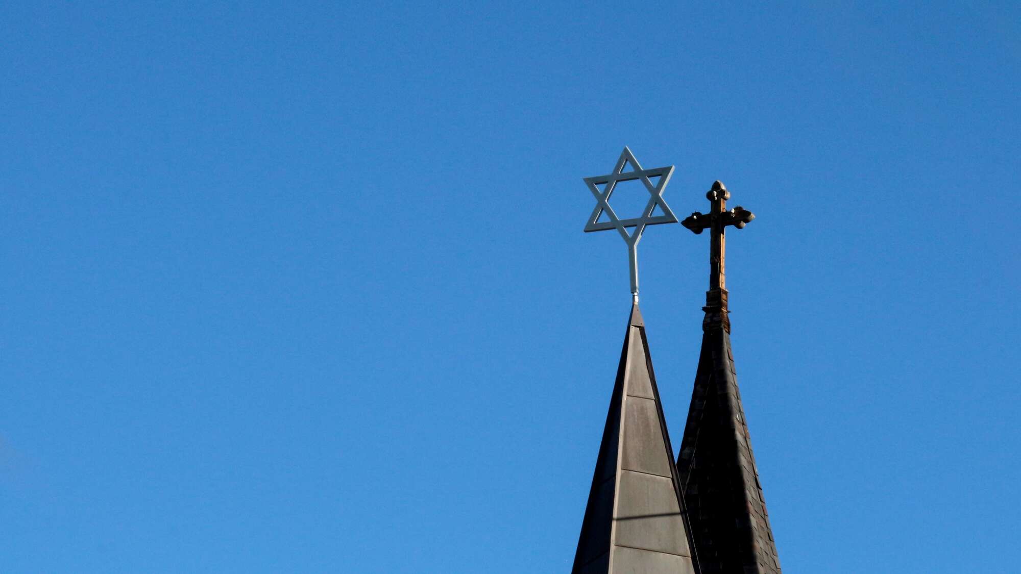 Die Türme einer Synagoge und einer Kirche nebeneinander vor blauem Himmel