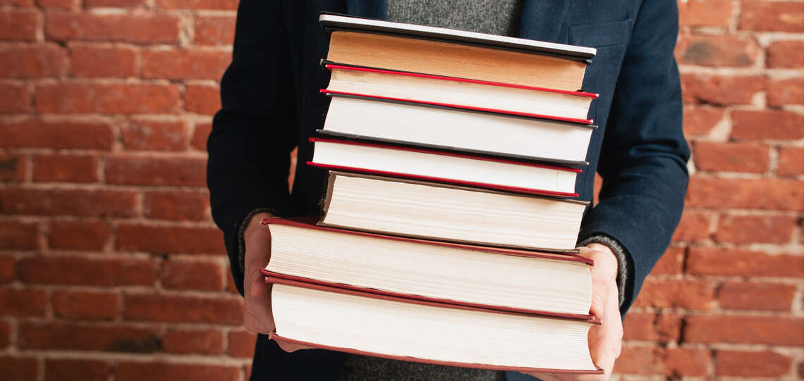 Man with a stack of books in is hands.